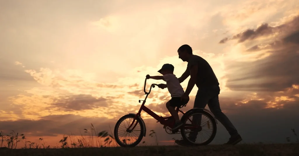 Silhueta de pai ensinando o filho a andar de bicicleta