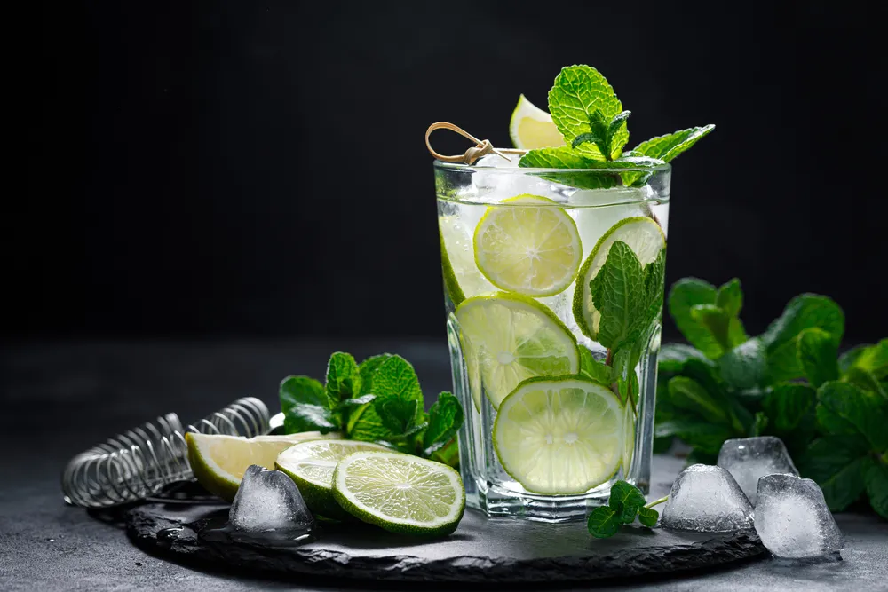Copo de mojito refrescante com limão siciliano, folhas de hortelã fresca e gelo sobre mesa escura, bebida tropical e saudável perfeita para o verão.
