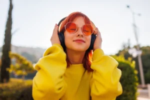 Retrato de uma menina com cabelo brilhante e piercings faciais que usa o telefone e escuta música em fones de ouvido. Menina adolescente ouvindo música em auscultadores sem fio enquanto caminhava pela cidade.
